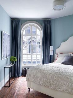 a bedroom with blue walls, white bedding and curtains on the window sill