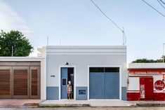 a woman is standing in the doorway of a small white and blue building with two garage doors