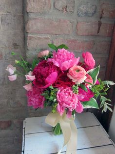 a bouquet of pink flowers sitting on top of a white table next to a brick wall