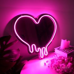 a heart shaped neon sign sitting on top of a table next to a pink light