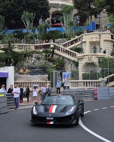 a black sports car driving down a street next to a building with stairs on it