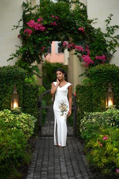 a woman is standing in front of some bushes and flowers, wearing a white dress