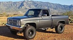 a gray truck parked in the dirt near mountains