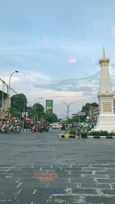 an intersection with a white clock tower in the middle and people on motorcycles parked nearby