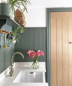 a white sink sitting under a wooden door next to a green wall and potted plants