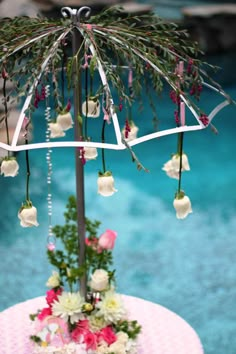 an umbrella decorated with flowers and greenery on top of a pink table next to a pool