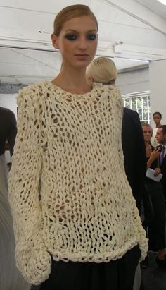 a woman in a white knitted sweater and black pants standing next to other people