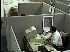 an office cubicle with a man sitting at a desk in front of a computer monitor