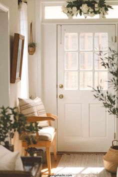 a white front door with flowers hanging from it's side and a chair in the foreground