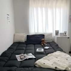 an unmade bed with a teddy bear on it in front of a window and white curtains