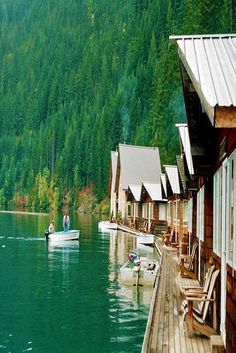 two people in a small boat on the water next to some houses and trees with mountains in the background