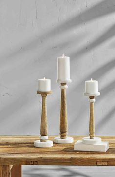 three wooden candlesticks with white candle holders on a wood table in front of a gray wall