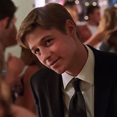 a young man in a suit and tie looking at the camera with other people around him