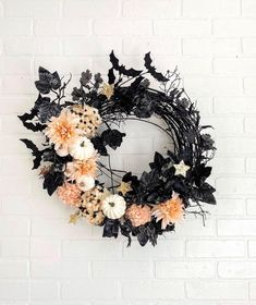 a black wreath with flowers and leaves hanging on a brick wall in front of a white brick wall