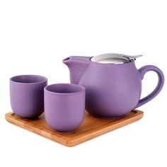 a purple tea set sitting on top of a wooden tray next to two cups and a spoon