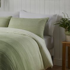 a bed with green comforter and pillows in a white room next to a plant