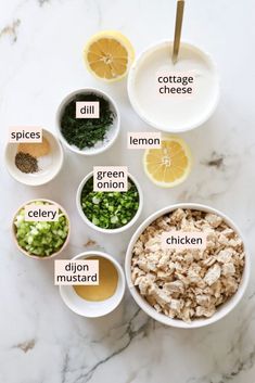 the ingredients for chicken salad laid out in small bowls on a marble countertop with lemons, celery, onion, and spices