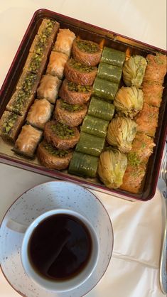 an assortment of pastries in a tray next to a cup of coffee on a table