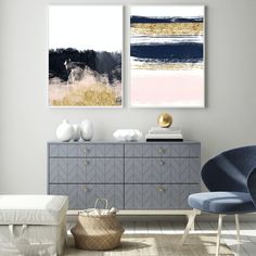 two paintings hang on the wall above a dresser in a living room with blue chairs