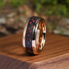 a ring with red and black speckles is sitting on top of a wooden surface