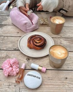 there is a cinnamon roll on the table next to two cups of coffee and other items