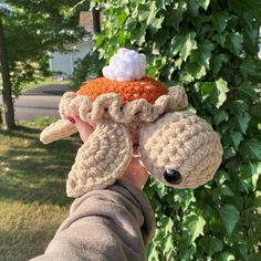 a person holding up a stuffed animal in front of a tree with leaves on it