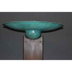 a large green bowl sitting on top of a wooden stand in front of a gray wall