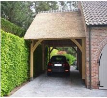 a car is parked in front of a house with a thatched roof and brick driveway