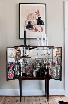 a bar cart with wine glasses and liquor bottles on it in front of a painting