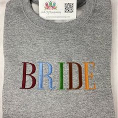 the bride t - shirt is grey with multicolored letters on it's chest