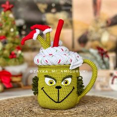 a knitted mug with a grin face on it and a christmas tree in the background