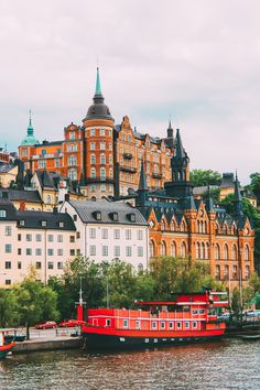 a red boat floating on top of a river next to tall buildings