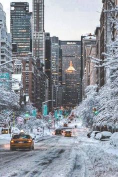 a city street covered in snow and surrounded by tall buildings with cars driving down it