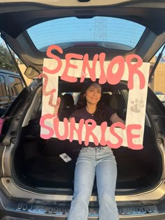 a woman sitting in the back of a car holding up a sign that says senior sunrise