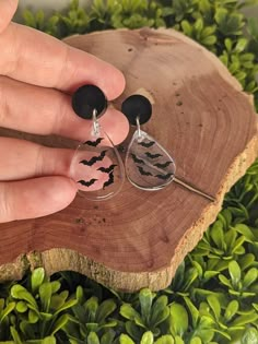 a person holding onto some black and white bats earrings on top of a piece of wood