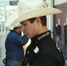 a man wearing a white cowboy hat looking down at his cell phone while standing in front of a building