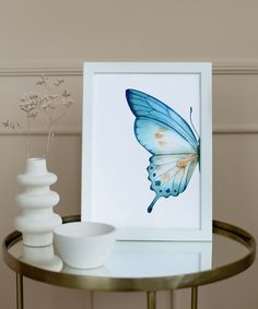 a blue butterfly sitting on top of a table next to a white bowl and vase