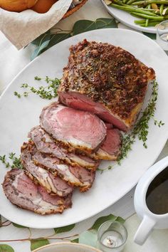 sliced meat on a white plate next to green beans and other food items in bowls