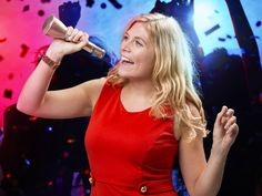 a woman in a red dress singing into a microphone with confetti on the background