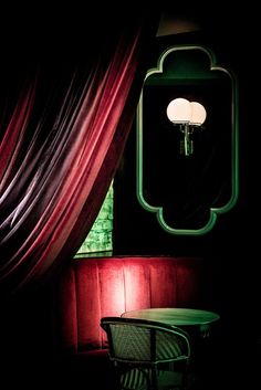 a table with a lamp on it in front of a mirror and red drapes