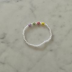 three smiley face beads on a white beaded bracelet with pink, yellow and green beads