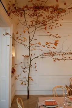 a dining room table with place settings and a tree in the center, painted white