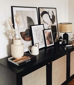 a black and white sideboard with pictures on it, vases and lamp in the corner