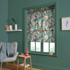 a living room with green walls and a window covered in floral print fabric, next to a gray chair