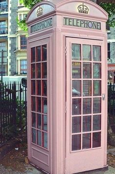 a pink phone booth sitting on the side of a road