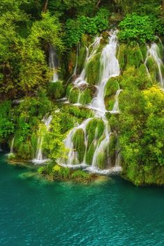 the waterfall is surrounded by lush green trees and blue water in this beautiful landscape photo