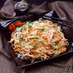 a black plate topped with pasta and veggies on top of a patterned table cloth