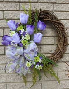 a wreath with purple flowers and greenery hanging on a brick wall