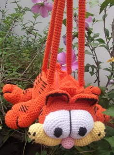 a crocheted stuffed animal is hanging from a plant with flowers in the background