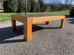 a wooden table sitting in the middle of a parking lot next to a tree and grass area